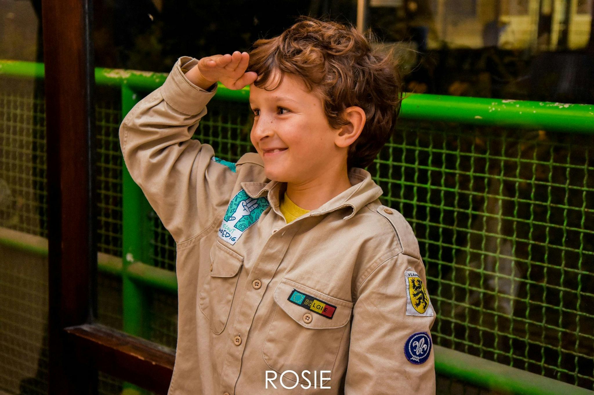 Lachende jongen doet de scouts groet in uniform 